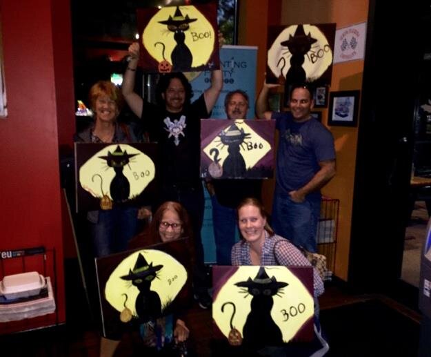 Guests holding up their finished paintings together at a themed Painting Party Events night.