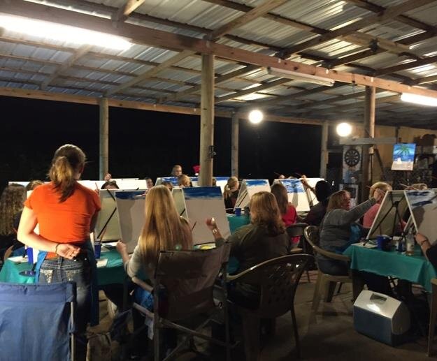 Guests painting together under a covered outdoor pavilion at a community Painting Party Events night.