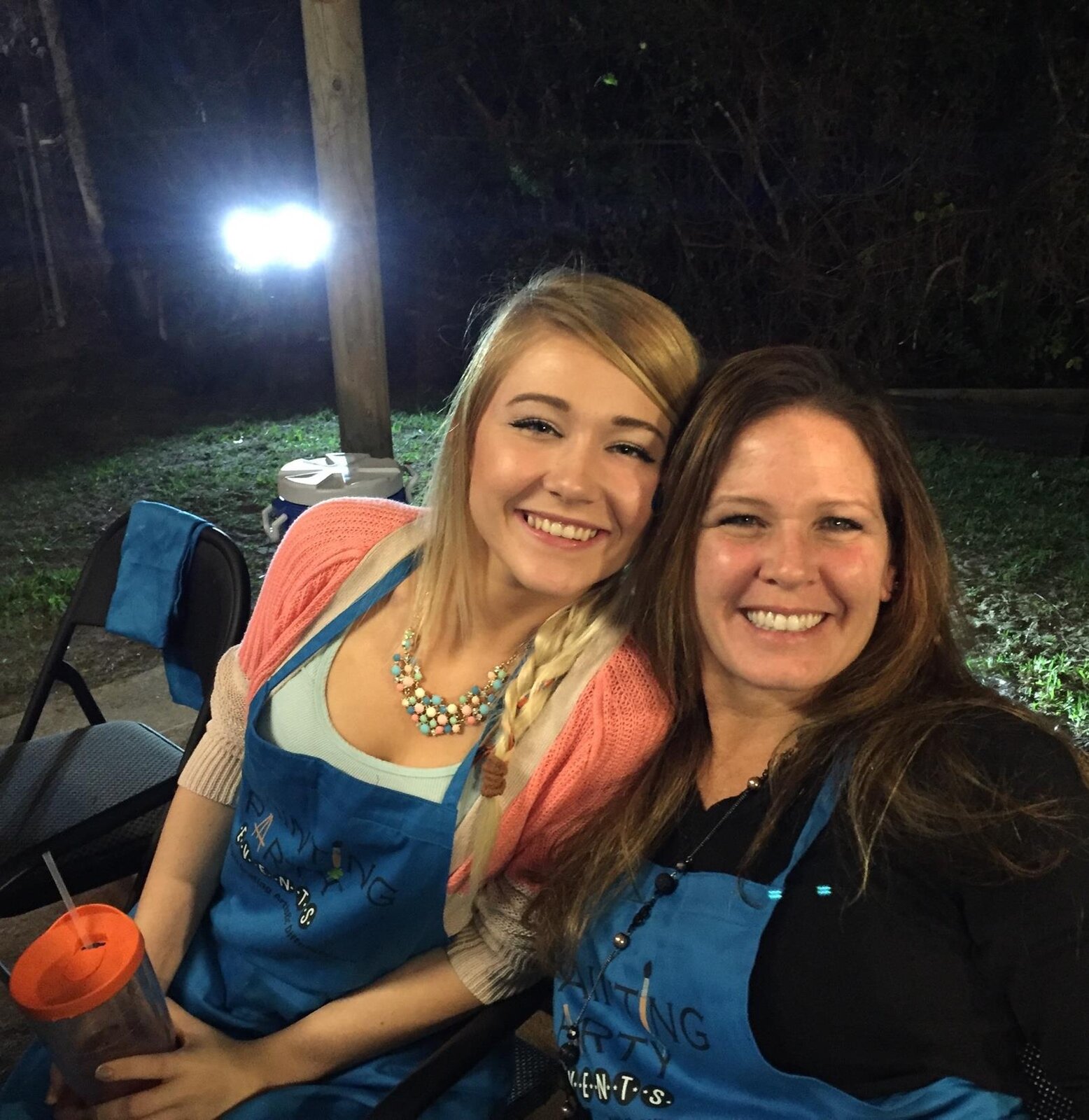 Two guests embracing and smiling in Painting Party Events aprons at an evening event.