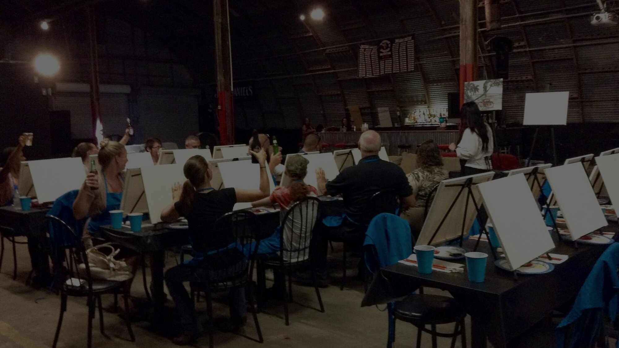 A full class of guests painting together at a Painting Party Events night, easels lined up under string lights.